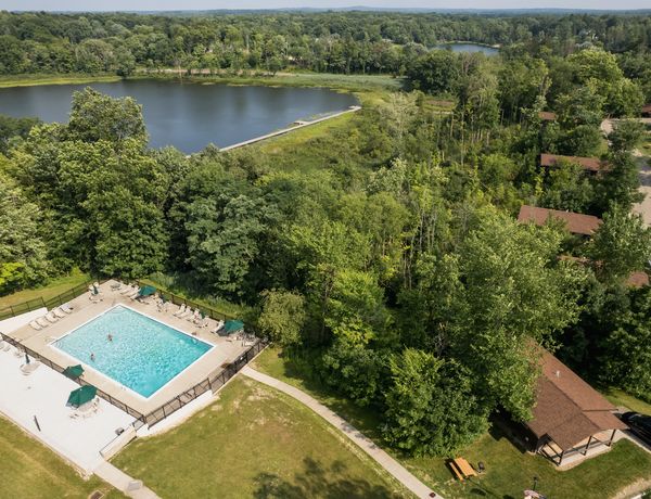 An aerial view of the resort's outdoor swimming pool and nearby guest cabins surrounded by lush green woods near the lake.