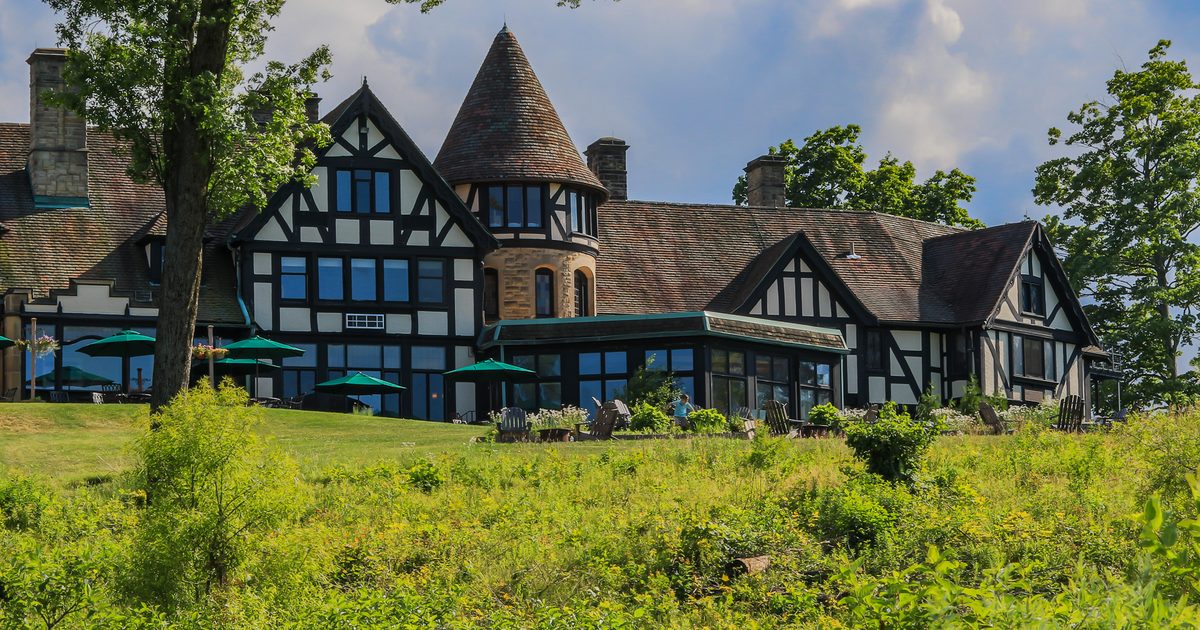 The historic, Tudor-style Punderson Manor building viewed from a hillside under a blue sky.